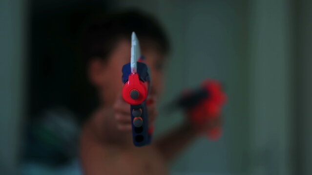 Young boy aiming colorful toy blasters toward camera during imaginative indoor play capturing childhood fantasy, excitement and playful pretend action at home