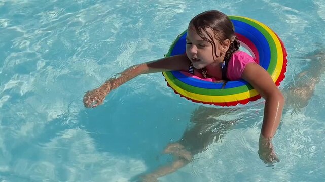 Girl swimming in pool with rainbow float on a sunny day