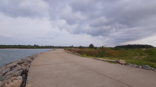Rear view of a lone man walking along a concrete coastal causeway beneath dramatic storm clouds.