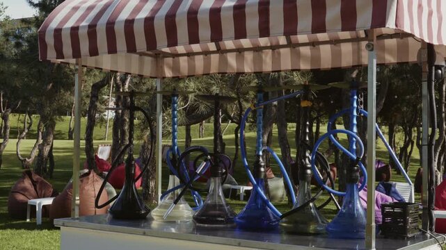 Hookahs with water stand in a row on a counter in the park with a recreation area in the background