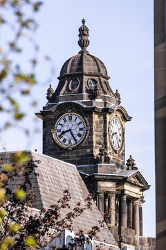 View of the historic Lancaster Town Hall clock tower with its ornate stone dome and Roman numeral clock face under a clear blue sky in Lancaster, England, United Kingdom.