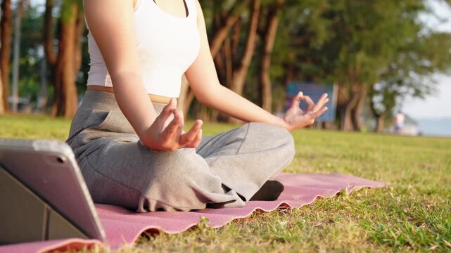 Close up Asian woman hands performing lotus pose in meditation, focusing on breath control in morning park. Hands person practicing yoga while sitting on yoga mat with sunrise for concept wellness 