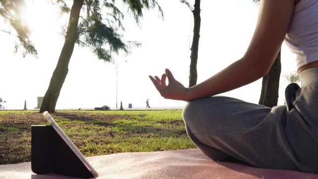 Close up Asian woman hands performing lotus pose in meditation, focusing on breath control in morning park. Hands person practicing yoga while sitting on yoga mat with sunrise for concept wellness 