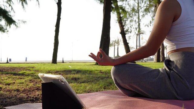 Close up Asian woman hands performing lotus pose in meditation, focusing on breath control in morning park. Hands person practicing yoga while sitting on yoga mat with sunrise for concept wellness 