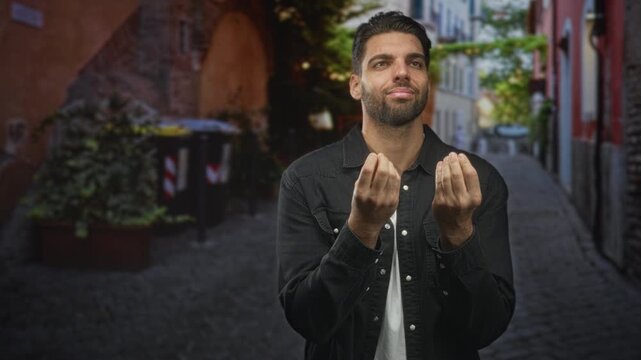 Man with cupped hands pleading gesture on a cobblestone street, beard visible and palms raised; quiet hope.
