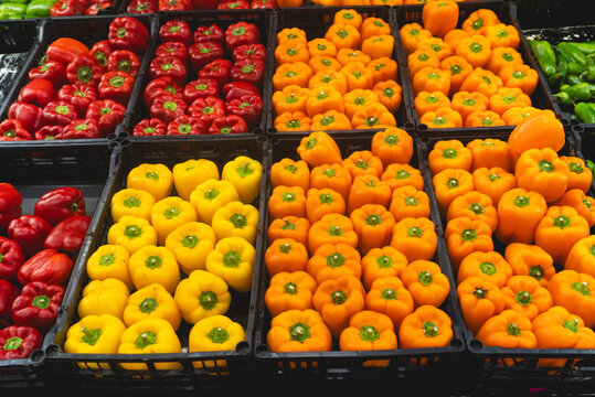 Abundant Display of Fresh Red, Yellow, and Orange Bell Peppers in Black Crates at a Market
