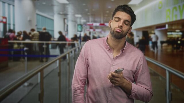 Man holding smartphone with head tilted and eyes closed in an airport queue leaning against railing; fatigue waiting.