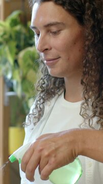 Vertical video: Squeezing green spray bottle, plant caretaker misting plants at home in white tee