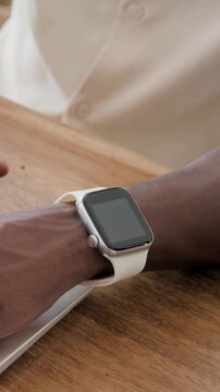 Vertical video: Starting, shifting left arm and wrist typing at desk near laptop with watch, shirt