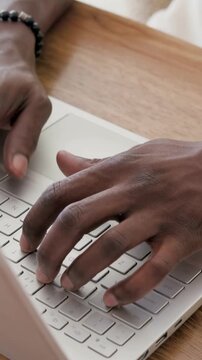 Vertical video: Framing male hands typing on laptop at home desk, with beaded bracelet
