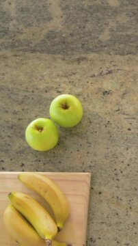 Vertical video: Panning green apple pair sitting on countertop, revealing bananas on board, bowl