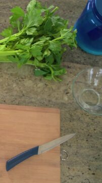Vertical video: Shifting bunch of celery during pitcher and bowl entering on countertop, for prep