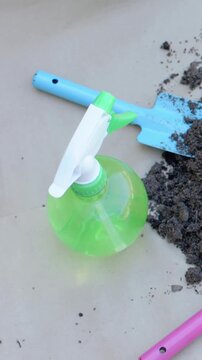 Vertical video: Rotating camera revealing green bottle centered on tray, trowel, soil, pink handle
