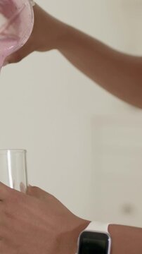 Vertical video: Tilting hands pouring smoothie to fill glass from pitcher at home with watch, ring