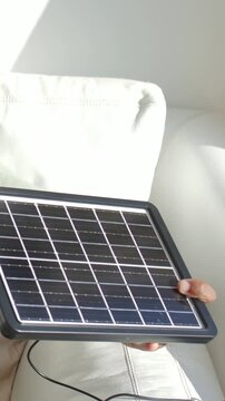 Vertical video: Adjusting man in mint shirt angling solar panel on couch chasing sunlight patch