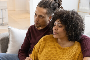 Obraz premium African American couple sitting closely on light-gray sofa in modern living room, wearing sweaters