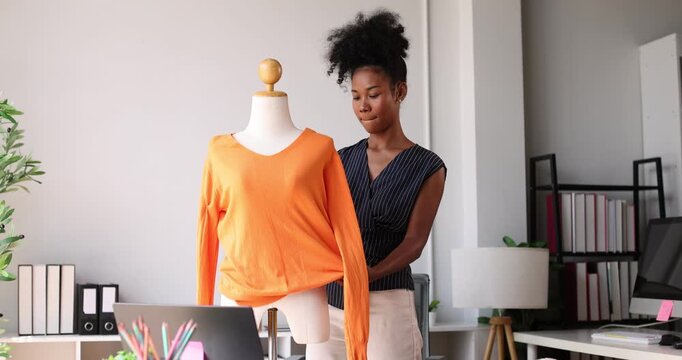 Young black female fashion designer measuring shirt on mannequin, creating new clothing designs in her studio, working with textile and apparel for future collection