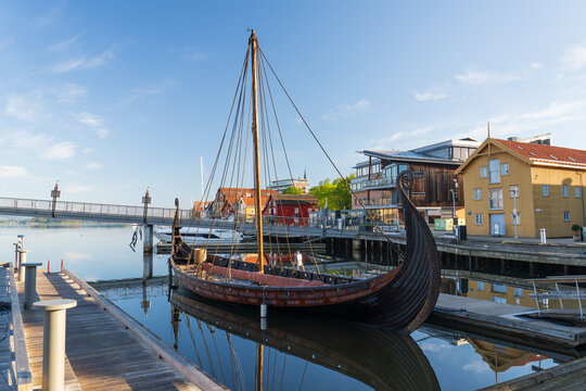 View of the Saga Oseberg Viking ship replica moored at the harbor with traditional wooden buildings and a modern bridge under a clear blue sky Tonsberg, Vestfold, Norway.