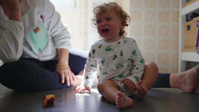 Crying toddler sitting on floor at home, emotional childhood tantrum moment with parenting challenges and family care concept