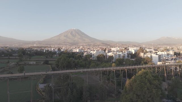 Drone rising over the historic Iron Bridge at sunset, revealing Arequipa cityscape and Misti Volcano backdrop, LOG footage
