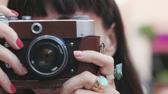 Close-up of a dark-haired woman holding a vintage camera near her face, looking through the viewfinder with focused expression. girl with a camera.