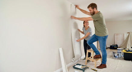 Fototapeta premium Smiling couple hanging wallpaper in a room. Home renovation and DIY project
