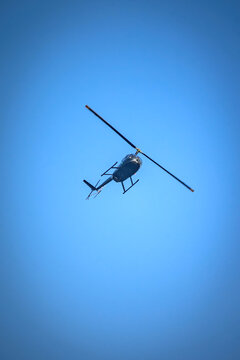 View of a dark helicopter flying through a clear blue sky in Rio de Janeiro, State of Rio de Janeiro, Brazil.