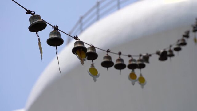 Traditional Buddhist prayer bell hanging on string outside Mindrolling Monastery in Dehradun, with blue sky and top of white stupa in the background
