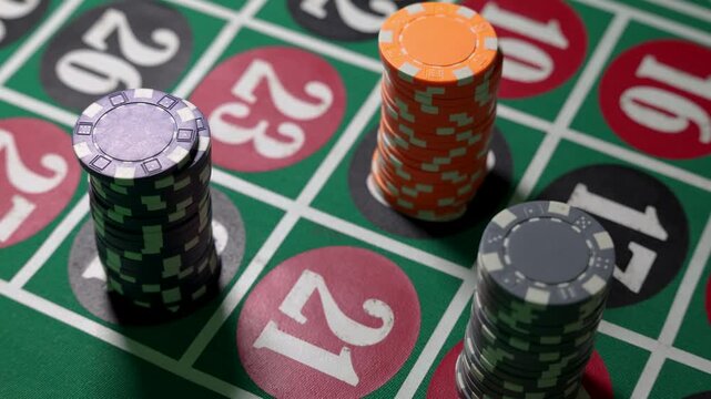 Stacks of casino chips positioned on a roulette table with visible numbered fields including 21. The chips differ in color and value and are arranged on specific betting areas. 