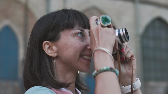 Close-up of a dark-haired woman holding a vintage camera near her face, looking through the viewfinder with focused expression. girl with a camera.