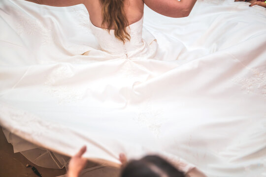 View of a bride in an elegant white wedding dress with a long embroidered train being spread out by hands in Rio de Janeiro, State of Rio de Janeiro, Brazil.
