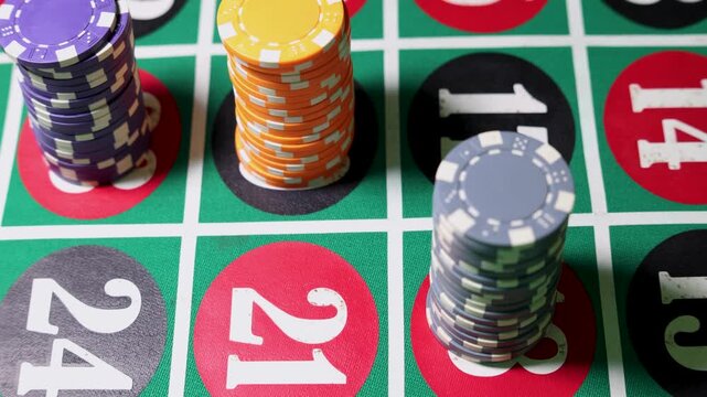 Stacks of casino chips are placed on roulette betting fields including 24, 21. The colored circles and printed numbers form a structured grid on the green table surface. 