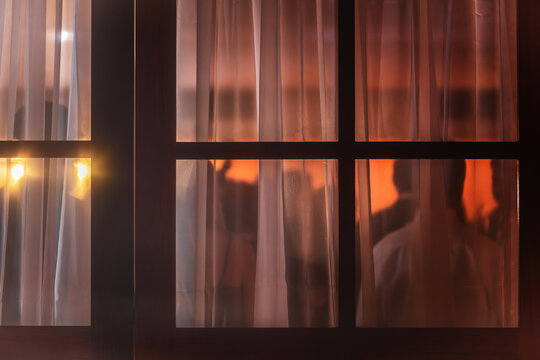 View of silhouettes of people at an indoor event seen through a window with white curtains and warm lighting Rio de Janeiro, State of Rio de Janeiro, Brazil.
