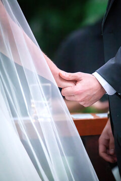 View of a bride and groom holding hands during a wedding ceremony with a white veil and dark suit in Rio de Janeiro, State of Rio de Janeiro, Brazil.