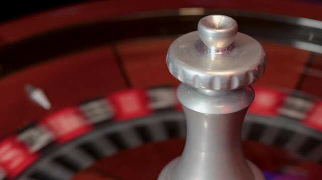 Roulette wheel in rotation with the central spindle visible above the circular track. A moving ball travels along the numbered pockets 