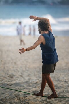 View of a man balancing on a slackline over the sand with the ocean in the background Rio de Janeiro, State of Rio de Janeiro, Brazil.