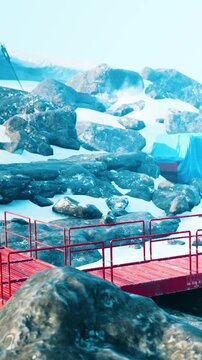 Workers are seen on a red platform near large rocks and snow. The setting is cold with visible ice formations in the background. The sun shines brightly over the scene.
