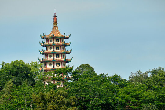 View of Pagoda Avalokitesvara rising above lush green trees under a clear blue sky in Banyumanik, Semarang, Central Java, Indonesia.