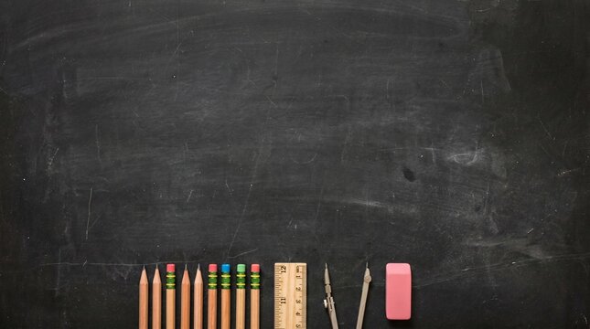 A clean chalkboard with various school supplies neatly arranged at the bottom. The supplies include pencils, a ruler, a compass, and an eraser