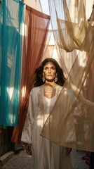 Obraz premium Beautiful adult woman stands among blowing colorful sheer curtains inside a sunlit narrow oriental street, exotic fashion lifestyle, travel inspiration concept.