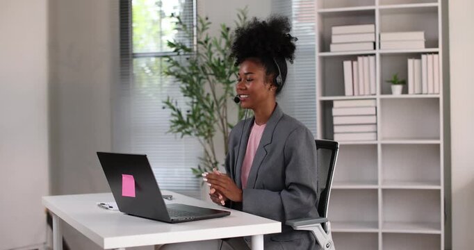 African american businesswoman smiling, wearing a headset with a microphone, providing online assistance and support while working from her home office setup