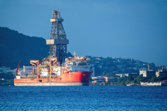 Niteroi, Brazil - 03 June 2026: View of the West Carina drillship anchored in the bay with the city skyline and lush green hills in the background under a clear blue sky.