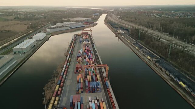 Aerial drone pull back over an active intermodal container terminal. Working gantry crane and reach stacker handling cargo at an inland port at sunset.