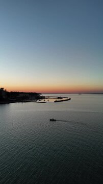 Vertical aerial view of a small boat cruising on Parana River at sunset with Posadas city skyline in the background.