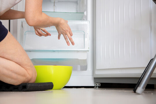 Person defrosts and cleans a freezer drawer at home, doing a household chore to maintain kitchen hygiene.