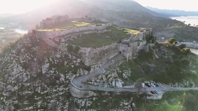 Aerial drone circle orbit shot around the outer defensive complex of Rozafa Castle in Shkod&euml;r, Albania, showcasing the stone entry paths, barbican gates, and rocky cliffs