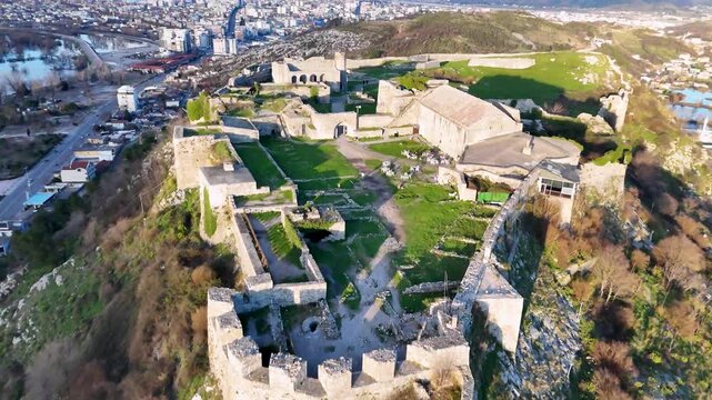 Aerial flies straight forward over defensive stone bastions toward the green courtyard and historic stone structures of Rozafa Castle in Shkod&euml;r, Albania