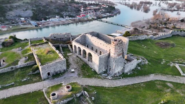 Aerial drone circle orbit shot over the historic Church of St. Stephen and mosque ruins inside Rozafa Castle, Shkod&euml;r, Albania, showcasing the fortress grounds and Buna River below