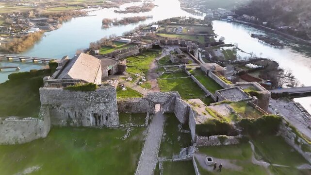 Aerial drone view over the ancient stone ruins of Rozafa Castle in Shkod&euml;r, Albania, showcasing the inner fort court, perimeter walls, and the merging Buna and Drin rivers