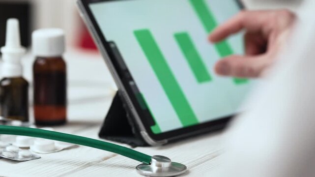 Doctor Looking at Green Pie Chart on Tablet with Selective Focus on Stethoscope on Table